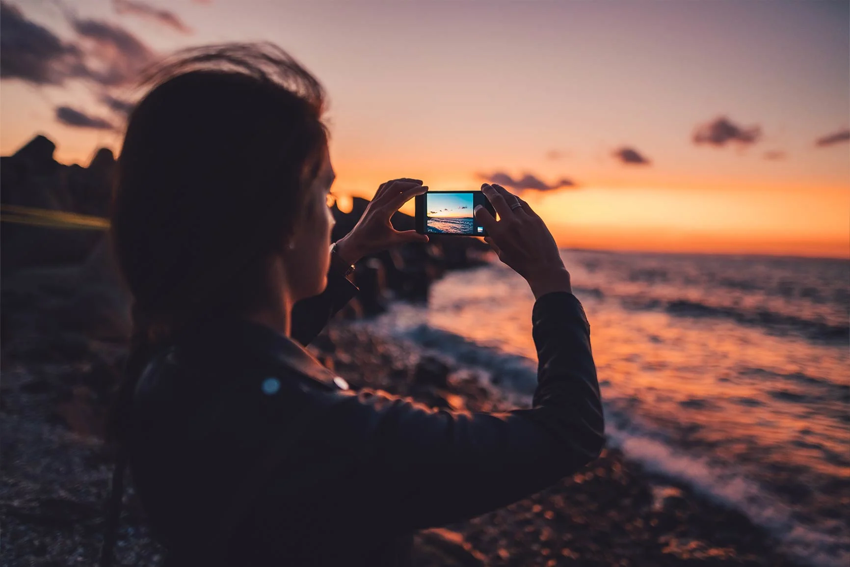 Person photographing sunset over the sea with a smartphone on the beach. Person photographing sunset over the sea with a smartphone on the beach.