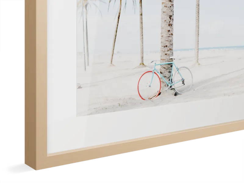 Corner detail of a framed photograph showing a light wood frame with white matting around an artistic beach scene image