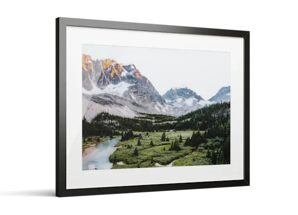 Framed photo print of a mountain landscape with snow-capped peaks, green valley, evergreen trees, and a turquoise river.