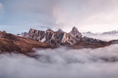 Mountain range above a blanket of clouds A mountain range with rugged peaks rising above a blanket of clouds in subdued light.