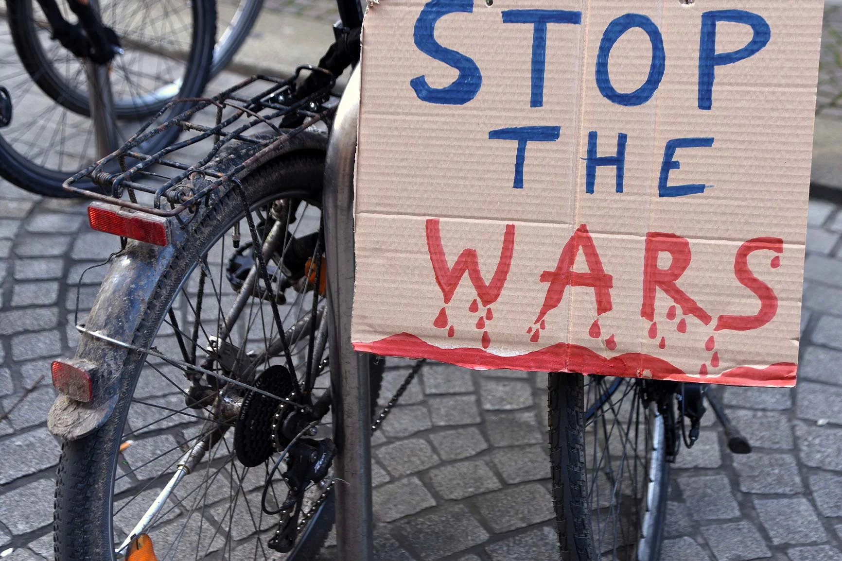 Bicycle with a cardboard sign: Stop the wars A close-up of a bicycle with a cardboard sign that reads “STOP THE WARS” in blue and red letters.
