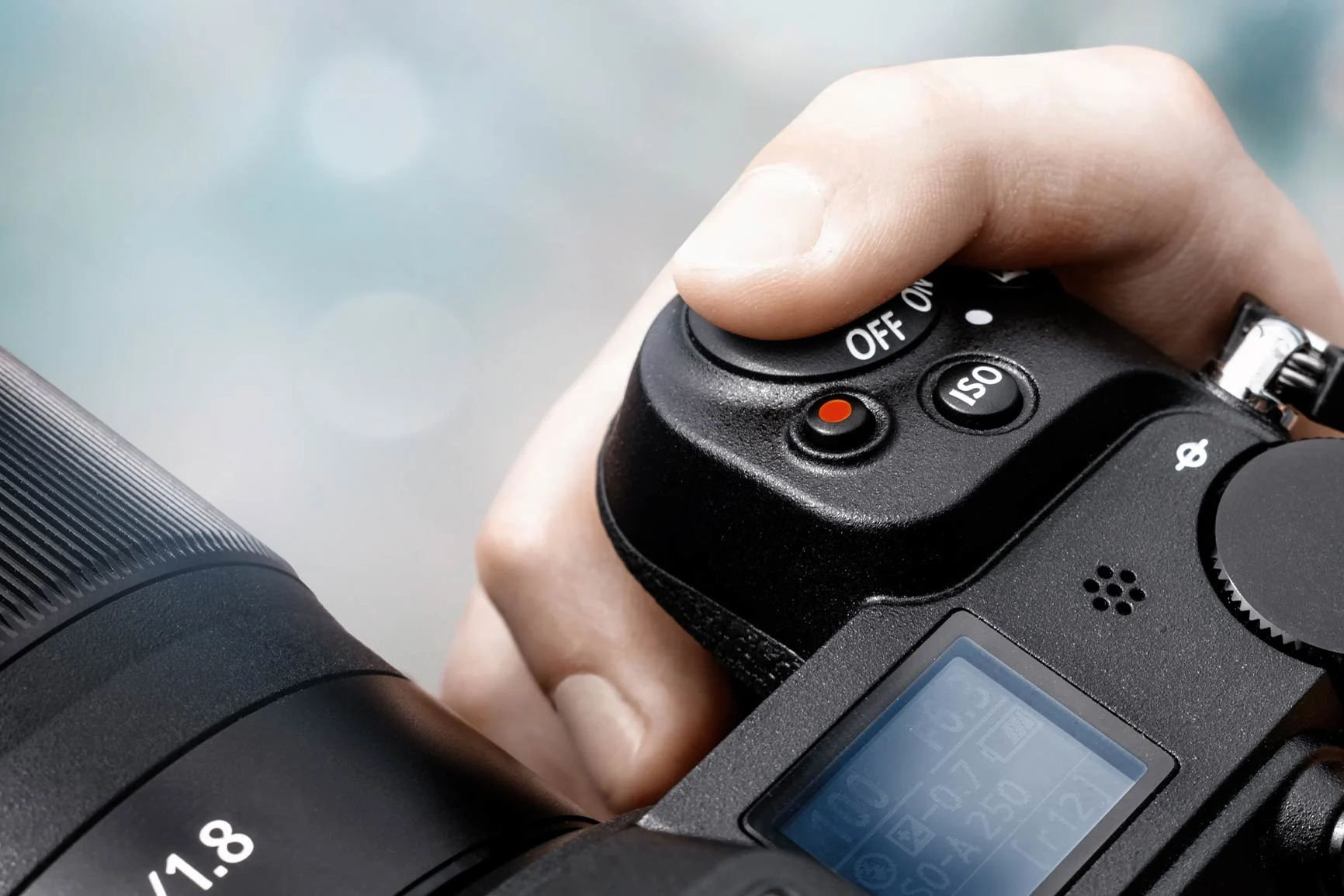 A hand is holding a camera A hand is holding a camera with a visible shutter button, ISO dial, and on/off switch.