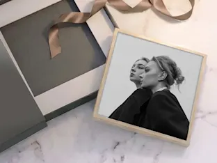 Une photo encadrée en noir et blanc de deux femmes, dans une boîte cadeau grise avec un ruban doré, présentée sur une surface en marbre.