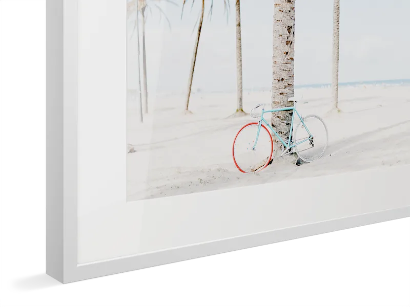 Close-up of white Magnet Frame with light blue vintage bicycle with red wheels leaning against a palm tree on a bright, sandy beach