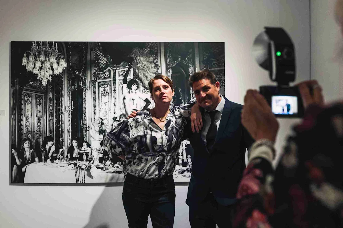 Deux personnes posent devant un tableau Deux personnes posent devant une grande photo en noir et blanc, une troisième personne les photographie.