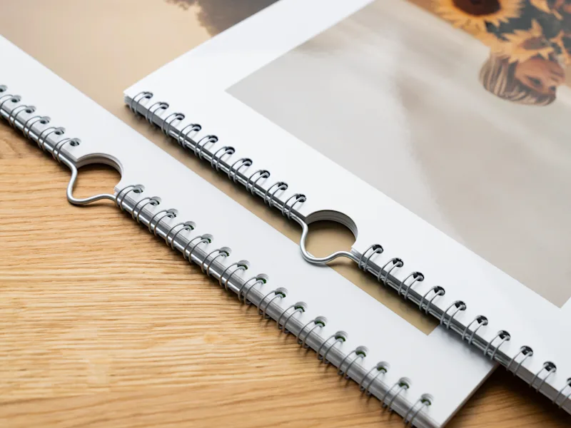 Fotokalender Spiralgebundene Fotokalender mit Metallspiralbindung auf einer Holzoberfläche liegend, mit Sonnenblumen im Hintergrund