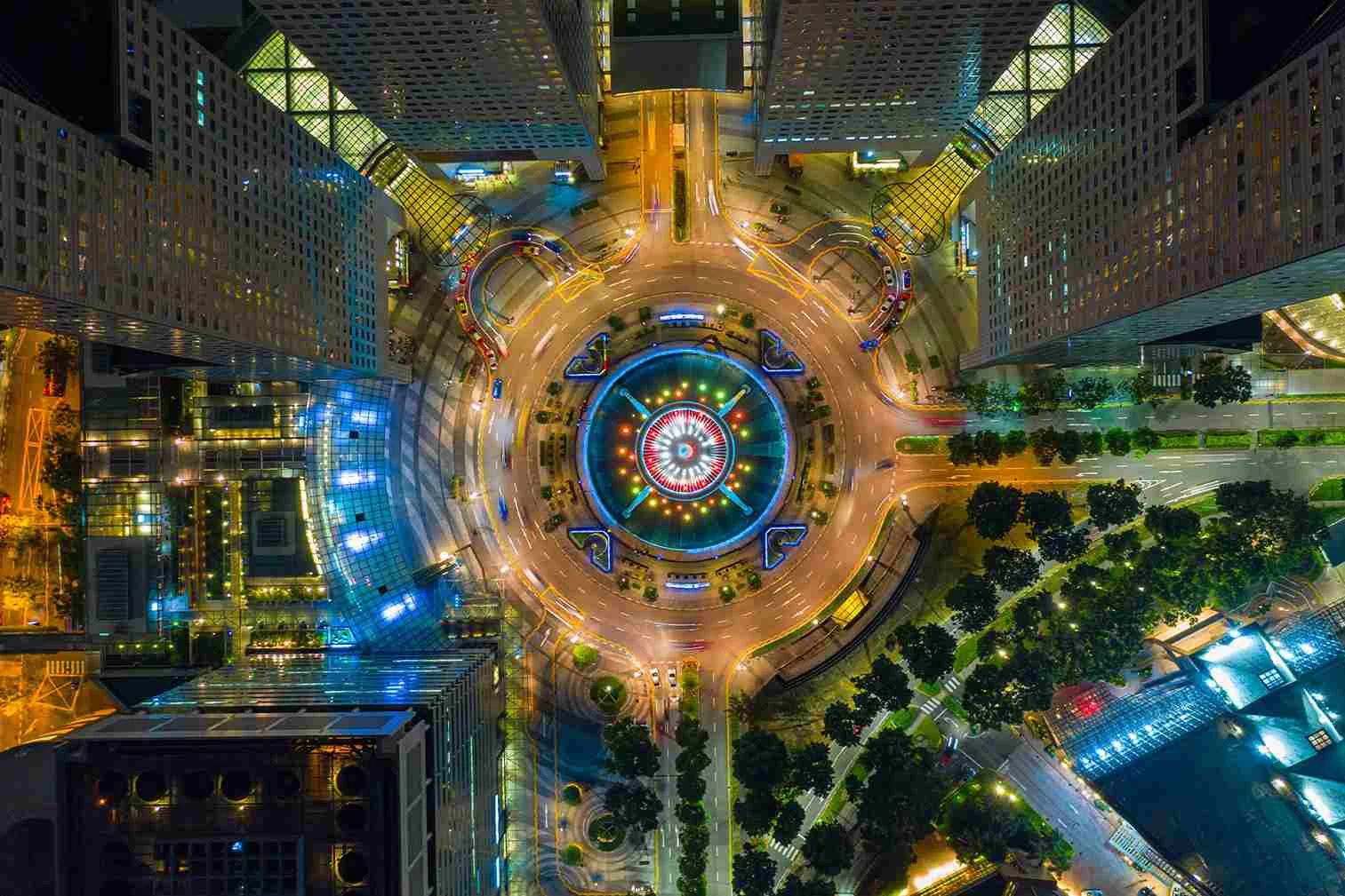 Bird's-eye view of a roundabout A bird's-eye view of a lit roundabout surrounded by high-rise buildings and streets in a city at night.