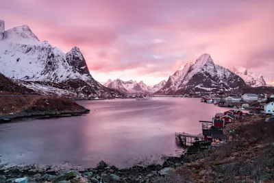 Mise au point et profondeur de champ 2 Fjord avec des montagnes, des maisons rouges, un ciel rose et une étendue d'eau, des sommets enneigés en arrière-plan.
