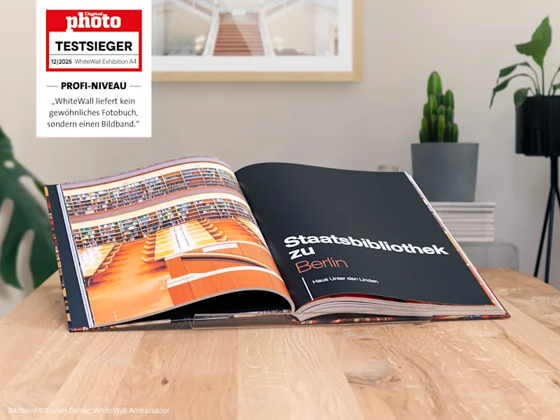 Bildband Fotobuch auf einem Holztisch geöffnet, mit Fotos der Berliner Staatsbibliothek; Pflanzen und Fotorahmen im Hintergrund.