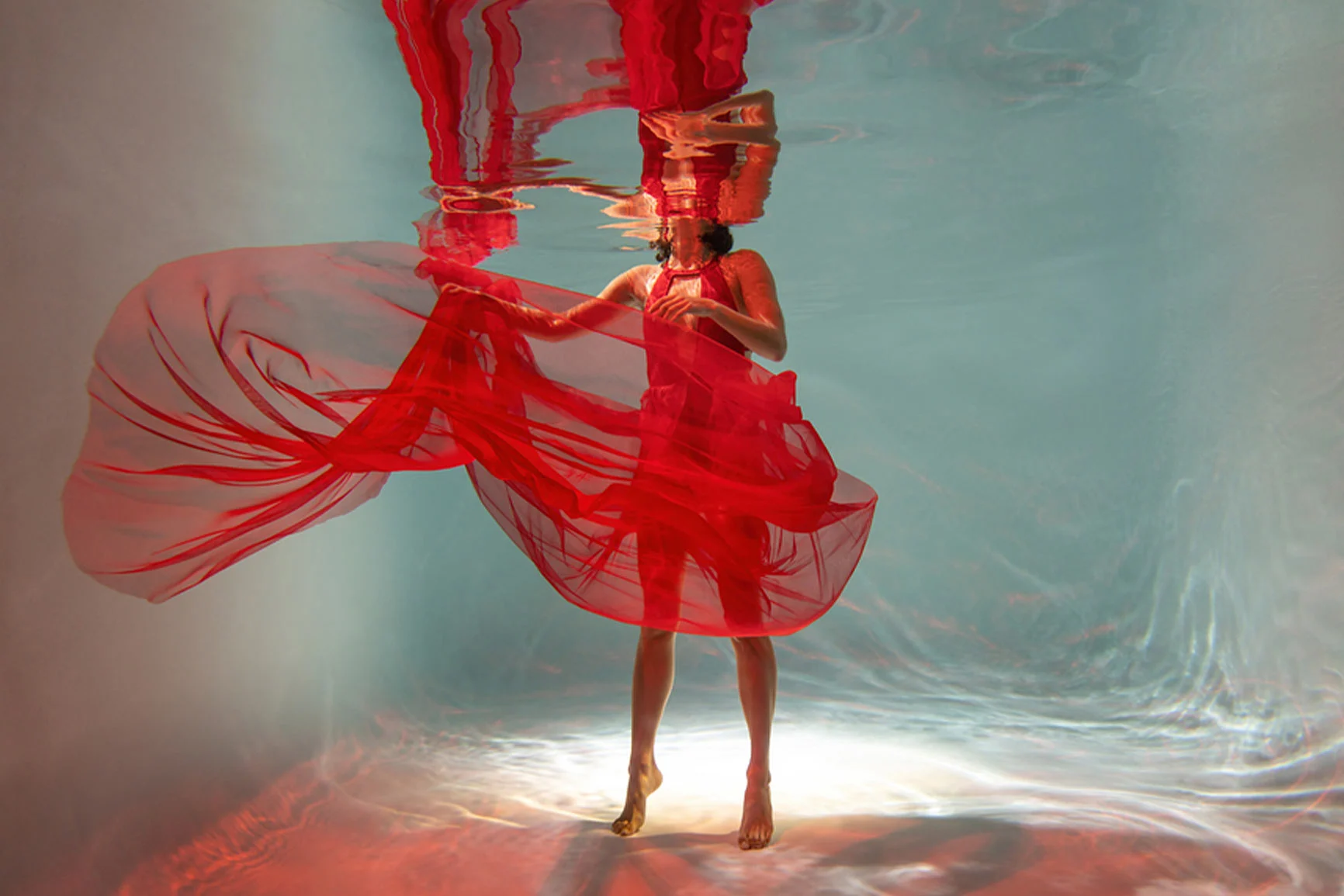 Una mujer con un vestido rojo baila bajo el agua, el vestido flota a su alrededor. Una mujer con un vestido rojo baila bajo el agua, el vestido flota a su alrededor.