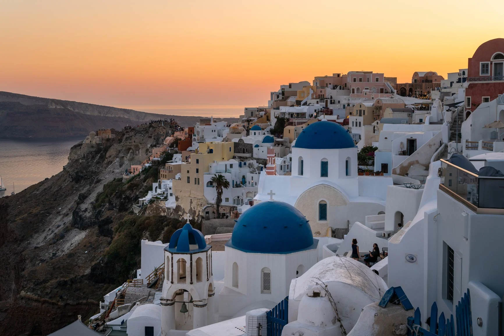 Vista de casas blancas con cúpulas azules en Santorini al atardecer junto al mar. Vista de casas blancas con cúpulas azules en Santorini al atardecer junto al mar.