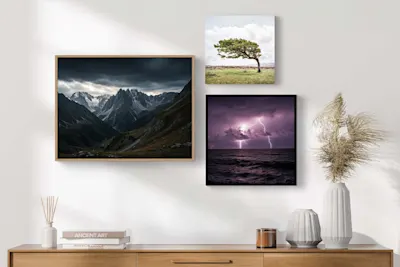 Weather photographs on a white wall Three weather photographs on a white wall, including a mountain landscape with dark clouds, a tree in a meadow, and a thunderstorm over the sea.