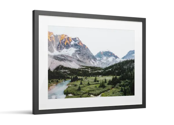 Framed photo print of a mountain landscape with snow-capped peaks, green valley, evergreen trees, and a turquoise river.