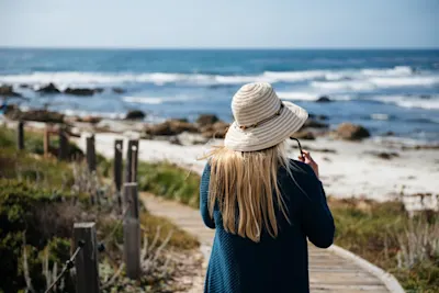 Strandbilder Frau mit Strohhut blickt auf das Meer, stehend auf einem Holzsteg am Strand.