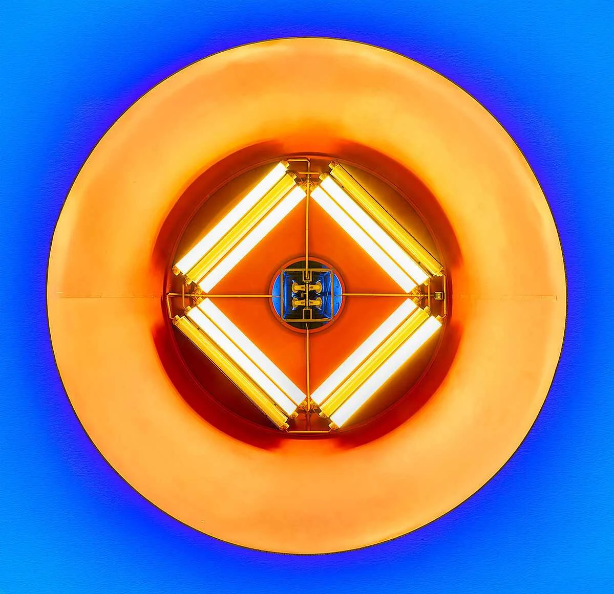 Close-up van een ronde oranje lamp met vier heldere witte buizen in een vierkante opstelling tegen een blauwe achtergrond. Close-up van een ronde oranje lamp met vier heldere witte buizen in een vierkante opstelling tegen een blauwe achtergrond.