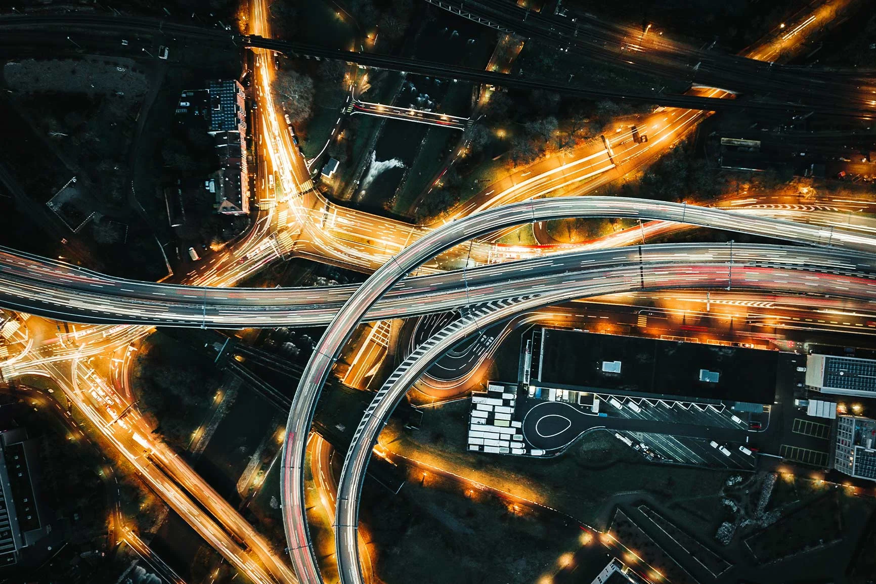 Luftaufnahme eines komplexen Autobahnkreuzes bei Nacht mit beleuchteten Straßen und fließendem Verkehr. Luftaufnahme eines komplexen Autobahnkreuzes bei Nacht mit beleuchteten Straßen und fließendem Verkehr.