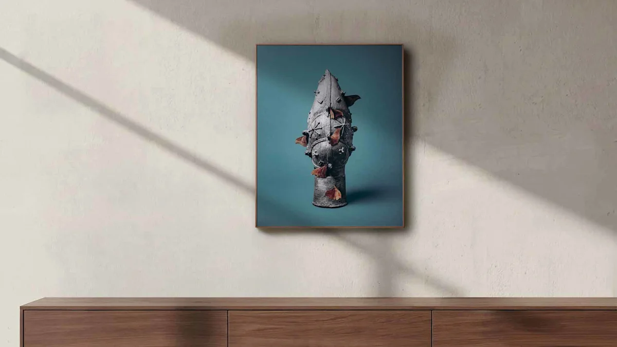 Framed wooden ArtBox on textured wall. The photograph shows the vertically oriented, light-framed artwork centered on a textured wall in beige tones. The piece itself displays the historic bronze sculpture with brown moths against a teal background. At the bottom of the image, the top edge of a modern wooden sideboard with visible grain anchors the scene. Soft diagonal shadows cutting across from the top left create a natural play of light and shade within the space.