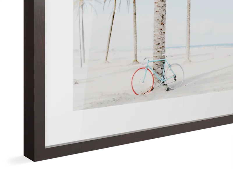 Light blue vintage bicycle with red wheel parked against palm trees on a bright sandy beach, framed in alder brown wood