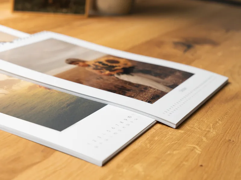 Fotokalender Mehrere gedruckte Fotokalender mit künstlerischen Landschaftsbildern und weißen Rändern, nebeneinander auf einer Holzoberfläche angeordnet