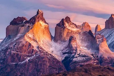 Mountain peaks with snow-capped slopes Rocky mountain peaks with snow-capped slopes beneath a pastel-colored sky.