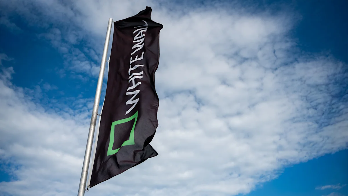 WhiteWall at the Horizonte Zingst Photo Festival A black flag with "Whitewall" text and a green square logo waves on a pole against a partly cloudy blue sky.