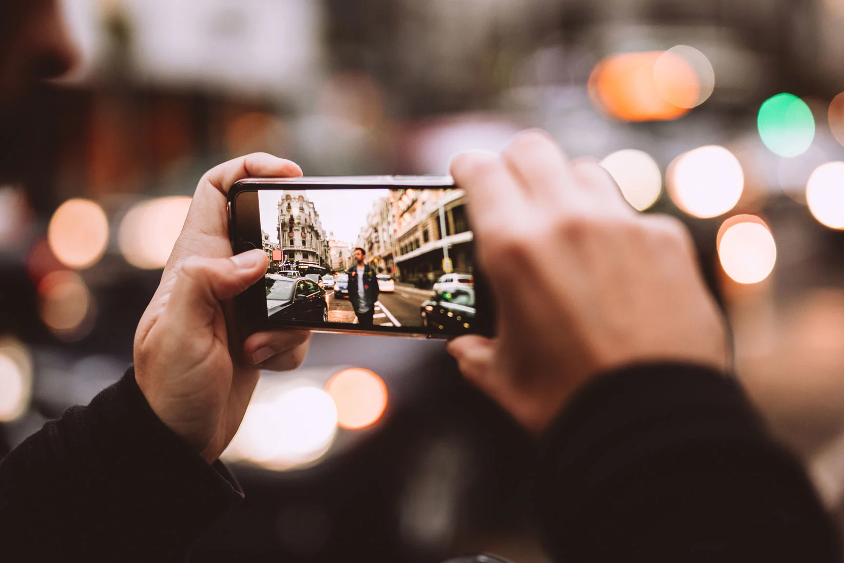 Person hält Smartphone und fotografiert eine belebte Straße mit historischen Gebäuden und Autos. Person hält Smartphone und fotografiert eine belebte Straße mit historischen Gebäuden und Autos.