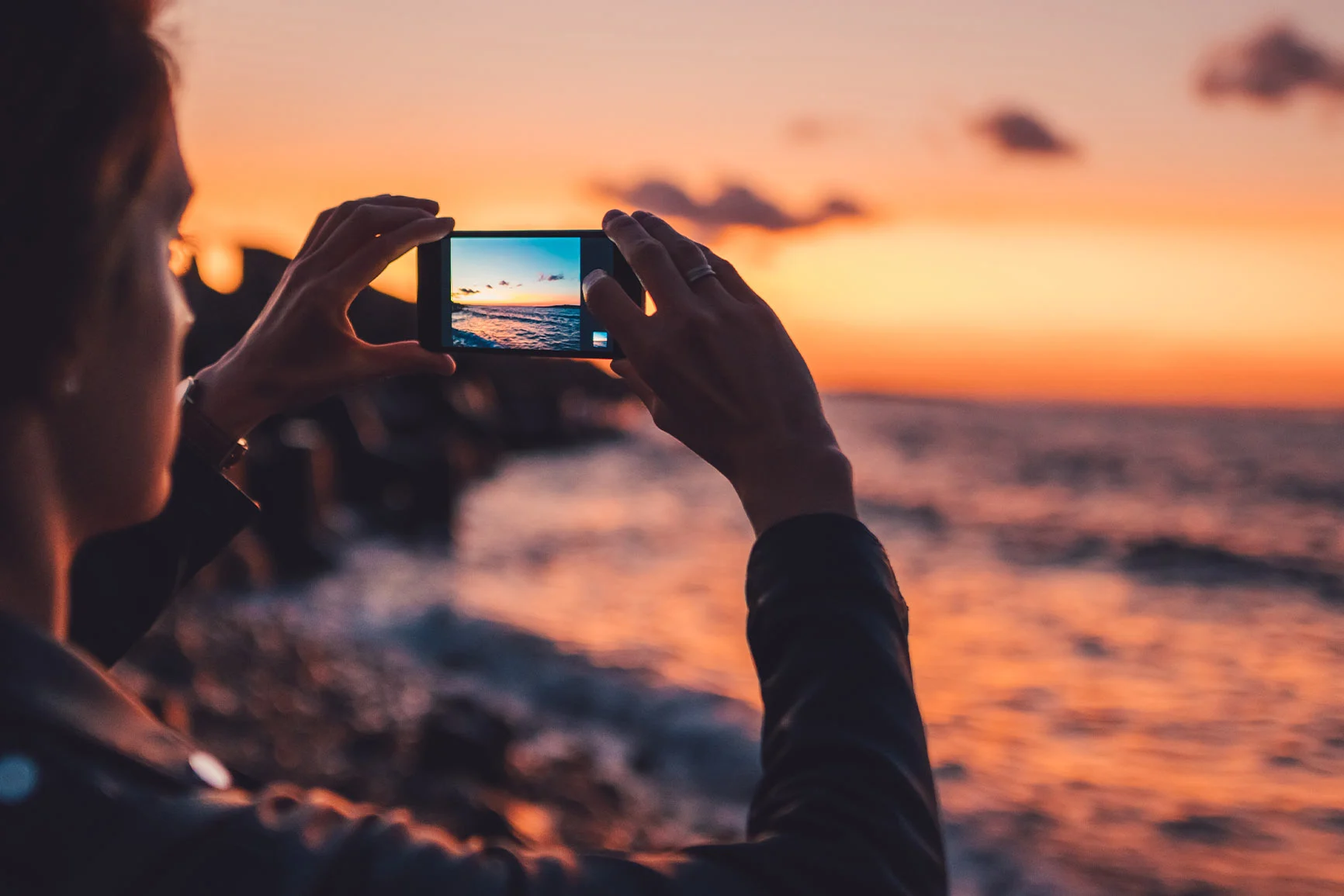 Une personne tient son smartphone et photographie le coucher de soleil sur la mer avec un ciel nuageux. Une personne tient son smartphone et photographie le coucher de soleil sur la mer avec un ciel nuageux.