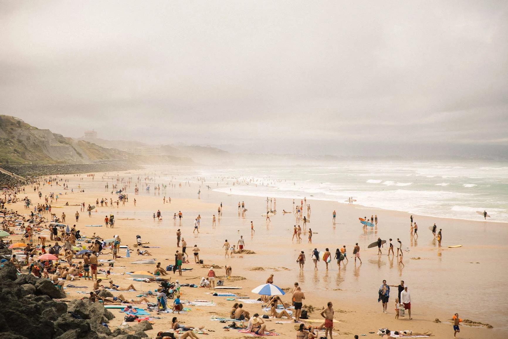 Playa abarrotada de gente relajándose junto al agua y en la arena bajo un cielo nublado. Playa abarrotada de gente relajándose junto al agua y en la arena bajo un cielo nublado.