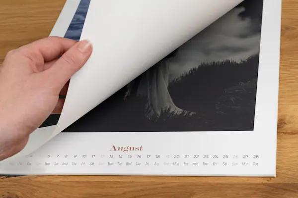 Photo Calendar Starting Month Hand turning page of wall calendar to reveal August month with dates and days displayed on wooden background
