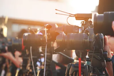 Several cameras with tripods and microphones A row of professional cameras mounted on tripods in sunlight, with microphones attached to the cameras.