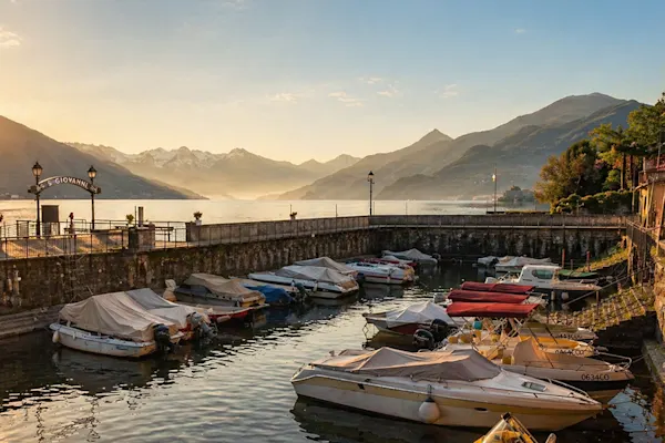 Kleiner Hafen vor Bergkulisse Kleiner Hafen mit mehreren Booten vor Bergkulisse bei Sonnenaufgang oder Sonnenuntergang.