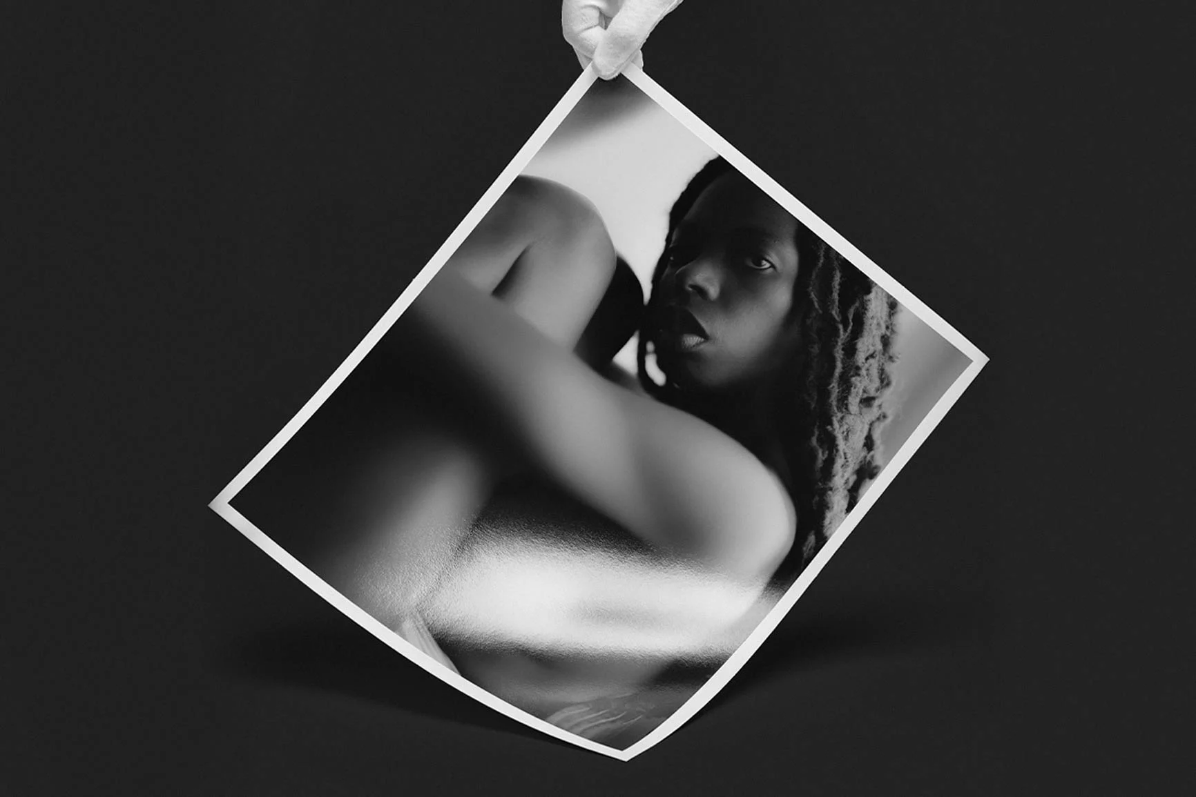 Fine Art Print Featuring a Nude Woman A hand is holding a black-and-white Fine Art Print depicting a nude figure seen from behind against a black background.