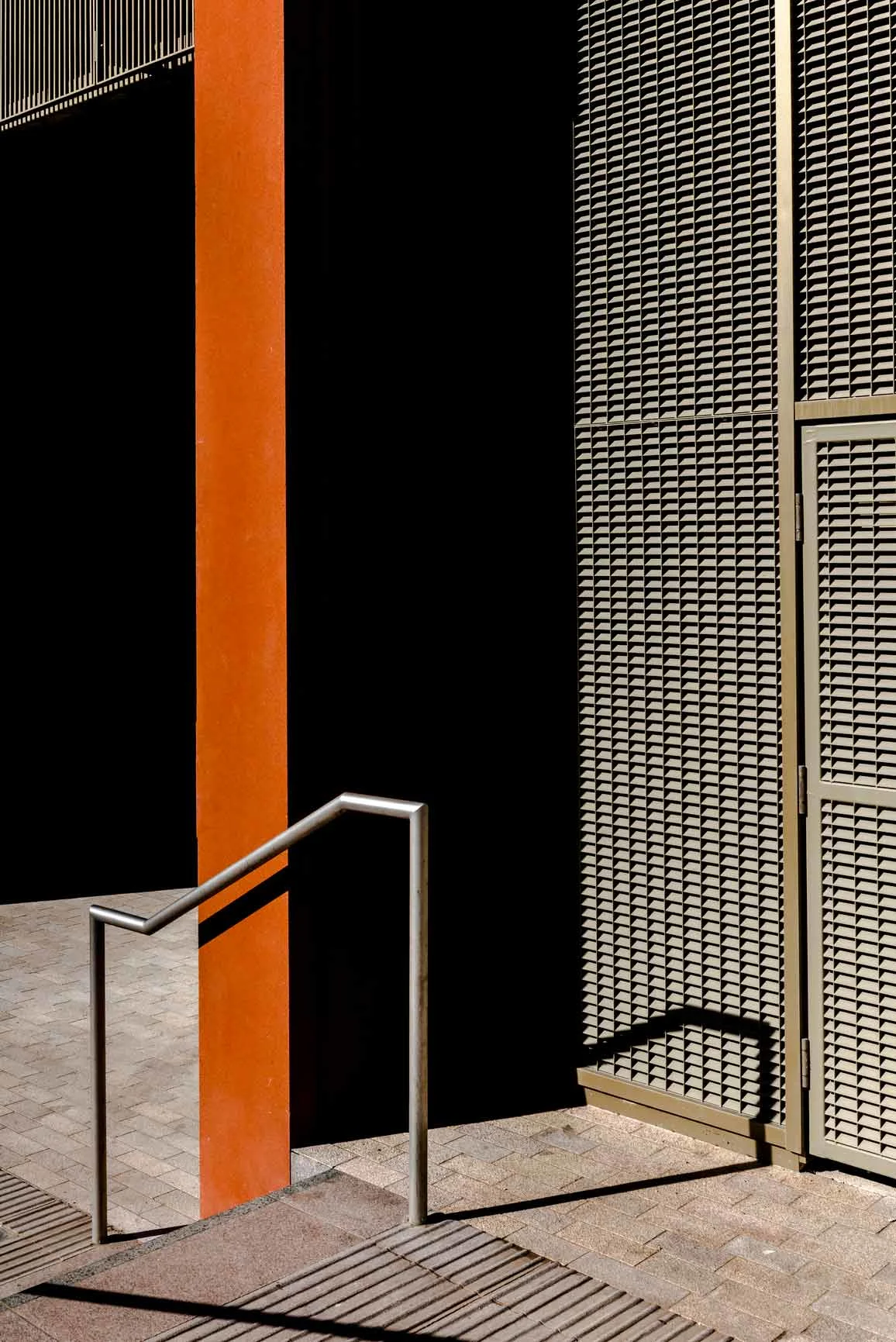 Pared naranja, superficie negra, rejilla metálica y una escalera con barandilla metálica a la sombra. Pared naranja, superficie negra, rejilla metálica y una escalera con barandilla metálica a la sombra.