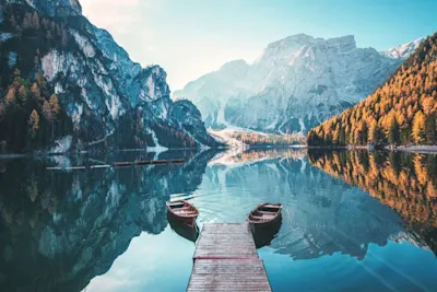 Mountain lake Wooden jetty with two rowboats on a tranquil mountain lake, surrounded by wooded and rocky mountains in autumn.