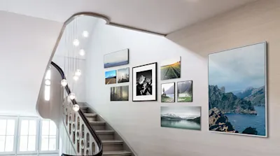 Bilder gekonnt aufhängen 8 Treppe mit Lampen, Wand mit mehreren Bildern in Petersburger Hängung, zeigen Landschaften und Architektur.
