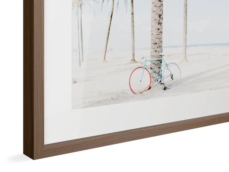 Light blue vintage bicycle with red wheel parked against palm trees on a bright sandy beach, framed in walnut colored wood