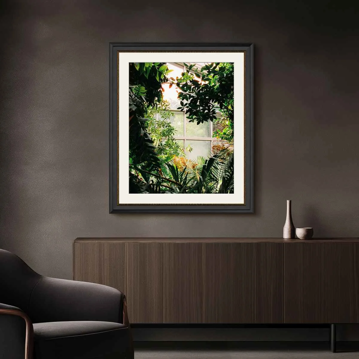 Photo in a passe-partout frame shows a window with green plants in front of it, on a dark gray wall above a sideboard. Photo in a passe-partout frame shows a window with green plants in front of it, on a dark gray wall above a sideboard.