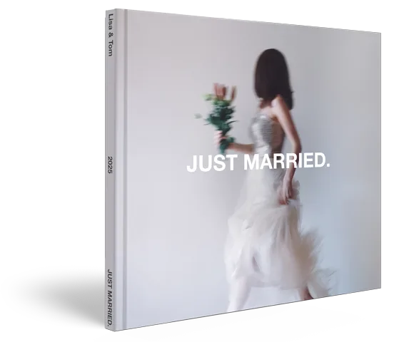 Coffee Table Book with linen cover showing a blurred bride in white dress holding flowers, with "JUST MARRIED." text overlaid on light gray background