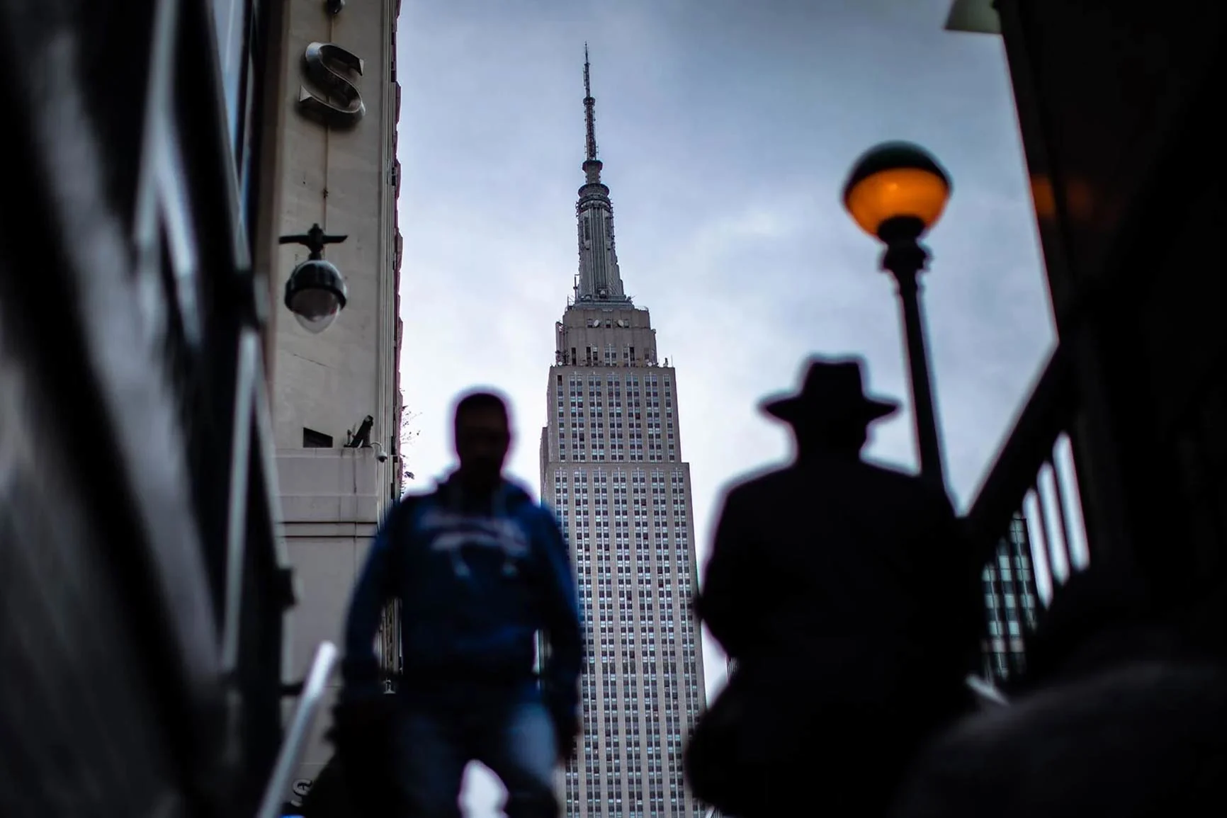 View of the Empire State Building A view of the Empire State Building with two blurry figures in the foreground and a streetlight on the right.