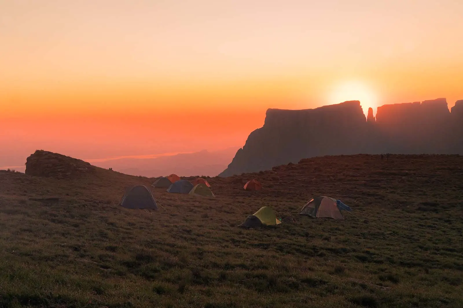 Tents standing in a mountainscape at sunset.