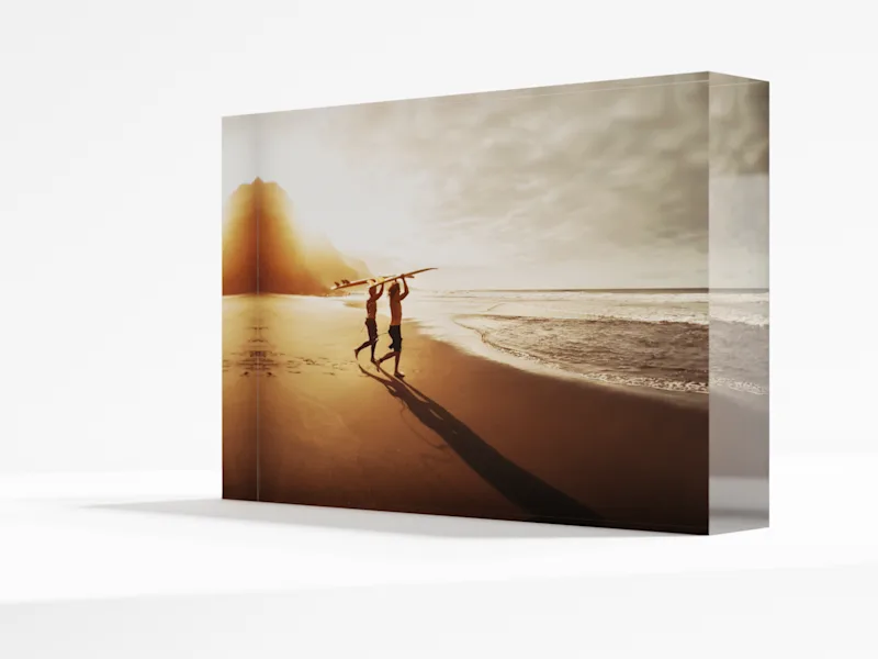 Foto-Acrylblock Silhouetten von Surfern, die bei Sonnenuntergang ihre Surfbretter an einem goldenen Strand entlangtragen, gedruckt auf einem Acryl-Fotoblock.