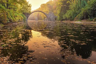 Simon Markhof - Herbstfotografie Steinbrücke über einen ruhigen, mit Herbstlaub bedeckten See