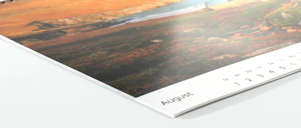 Foto-Kalender Inkjet matt Nahaufnahme einer Kalenderseite, die den August zeigt, mit einem verschwommenen Landschaftsbild im Hintergrund