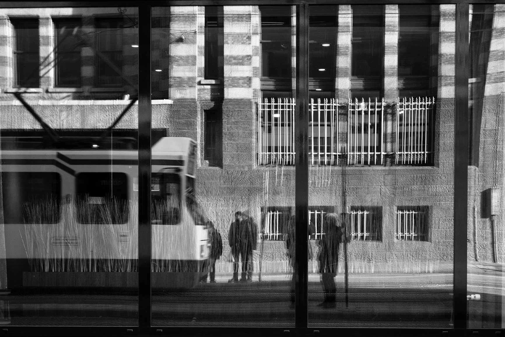 A black-and-white reflection of a tram A black-and-white reflection of a city tram and several people in front of a building.