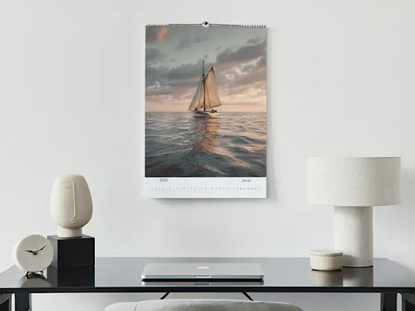 Wand-Fotokalender Moderner Schreibtischaufbau mit minimalistischen Keramiklampen, schwarzer Uhr, Laptop und Wandkalender mit Segelboot bei Sonnenuntergang