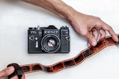 LP | Magazin | Inspiration | Product Grid Section | Auch interessant | Analoge Fotos digitalisieren | Grid #3 | Image Des mains tiennent une bande de film à côté d'une caméra zénithale sur une table blanche.