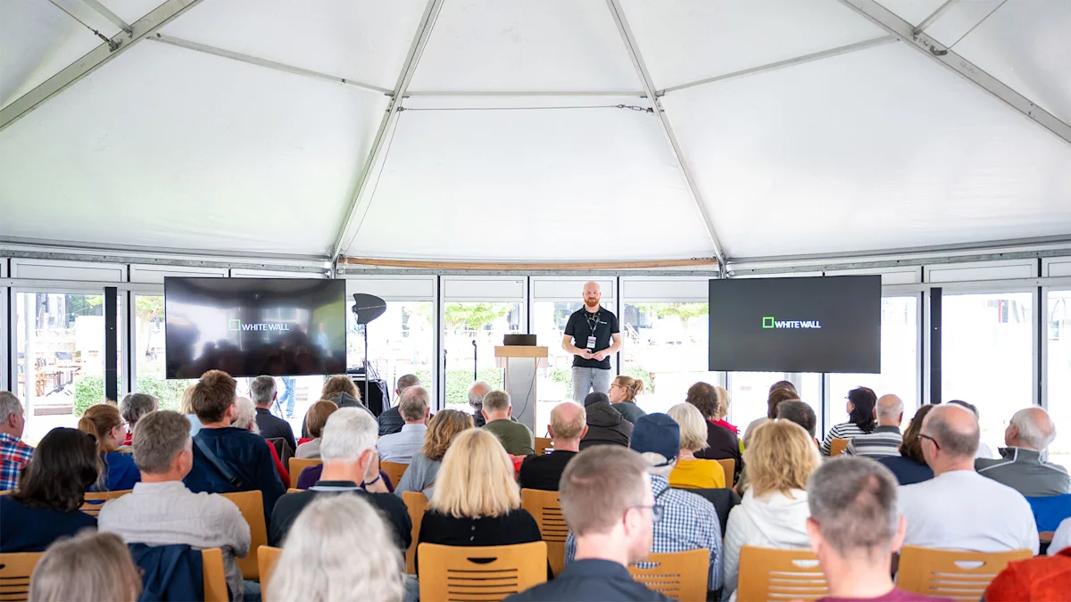 WhiteWall Expert Talk at the Zingst Photo Festival A speaker presents at a WhiteWall event inside a white tent, addressing a large seated audience with two display screens visible.