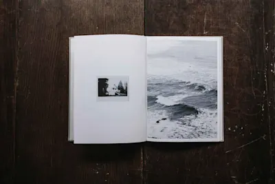 Livres et ressources en ligne pour les photographes 1 Livre ouvert, à gauche des bâtiments, à droite des vagues, sur une table en bois sombre.
