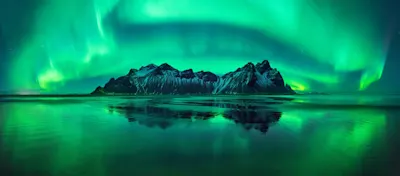 L'importance de la lumière en photographie 1 Des aurores boréales vertes au-dessus des montagnes enneigées qui se reflètent dans l'eau calme.