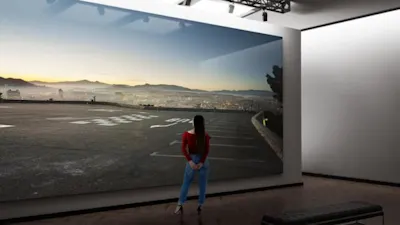 masterprint-teaser Frau steht vor einem WhiteWall Masterprint mit Stadtansicht bei Sonnenuntergang in einem Ausstellungsraum.